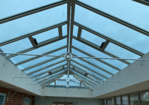 Glass conservatory roof with metal beams forming a pitched structure; blue-tinted glass panels and central ridge beam; part of Glaze Ltd project